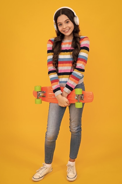 Estilo de vida adolescente da moda linda adolescente com skate e fone de ouvido isolado no fundo do estúdio Adolescente feliz e emoções positivas e sorridentes da adolescente