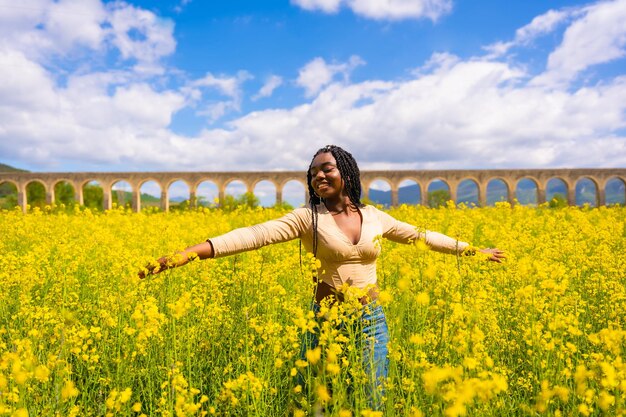 Estilo de vida apreciando a natureza em liberdade retrato de uma menina étnica negra com tranças em um campo de flores amarelas