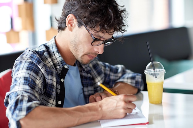 estilo de vida, criatividade, freelance, inspiração e conceito de pessoas - homem criativo com notebook ou diário escrevendo e bebendo suco no café