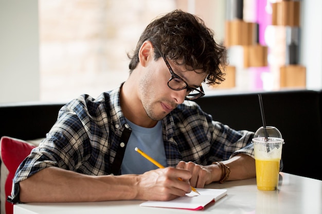 Foto estilo de vida, criatividade, freelance, inspiração e conceito de pessoas - homem criativo com notebook ou diário escrevendo e bebendo suco no café