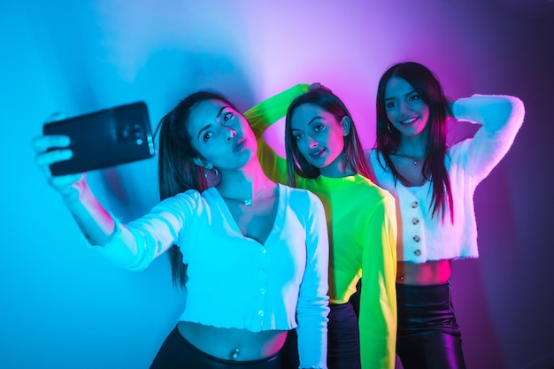 Estilo de vida de amigos festejando em uma boate com luzes de neon azuis e rosa tirando uma selfie com o telefone