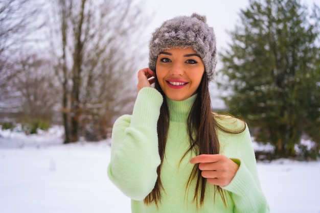 Estilo de vida de inverno, retrato jovem morena caucasiana com roupa verde e chapéu de lã, sorrindo na neve, férias na natureza