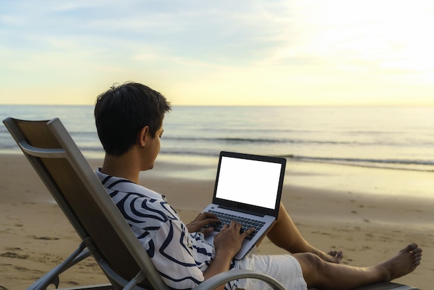 Estilo de vida de jovem blogueiro asiático trabalhando e usando o teclado no laptop enquanto está sentado na praia