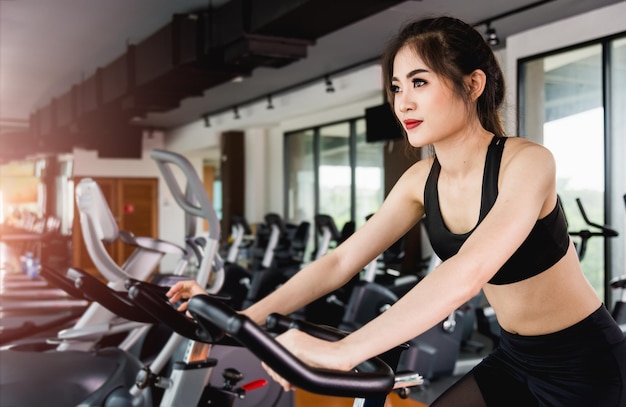 Estilo de vida de mulher usando equipamento de bicicleta ergométrica para treinamento de exercícios aeróbicos na academia de ginástica
