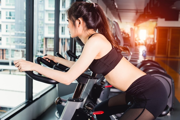Estilo de vida de mulher usando equipamento de bicicleta ergométrica para treinamento de exercícios aeróbicos na academia de ginástica