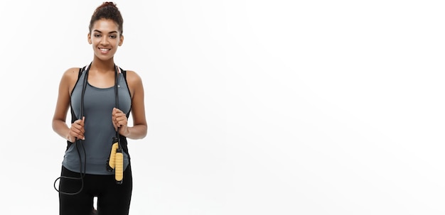 Estilo de vida de treinamento esportivo e retrato do conceito de Fitness de uma linda e feliz mulher afro-americana se exercitando com pular corda isolado no fundo branco do estúdio