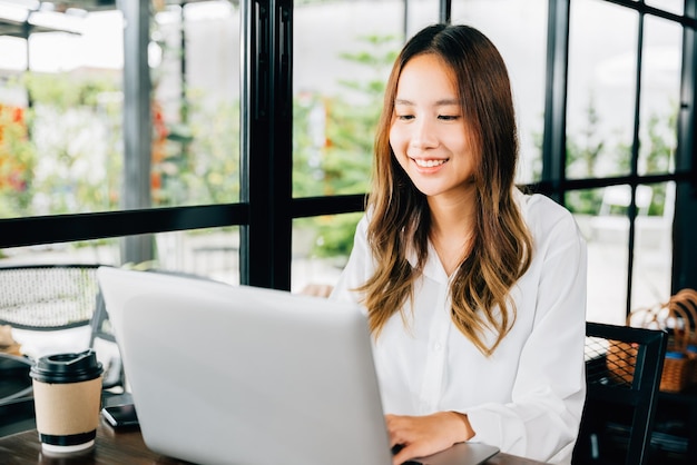 Estilo de vida de uma jovem empresária asiática usando laptop em uma cafeteria, feliz e lindo freelancer digitando teclado em laptop, trabalhando on-line fora do escritório