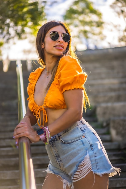 Estilo de vida de uma jovem morena caucasiana, caminhando no verão em um parque da cidade. Retrato da menina sorrindo na escada do parque