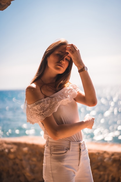 Estilo de vida de uma jovem ruiva caucasiana vestida de branco sobre uma rocha perto do mar em uma manhã de verão