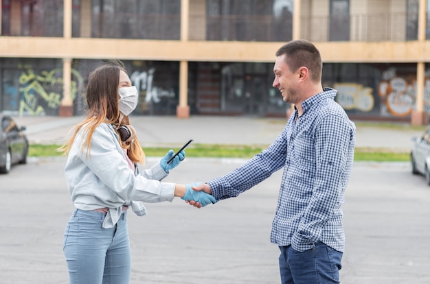 Foto estilo de vida durante a epidemia de doenças virais na europa. coronavírus covid-19, gripe. uma garota com uma máscara médica cirúrgica e luvas de um telefone nas mãos cumprimenta um jovem.