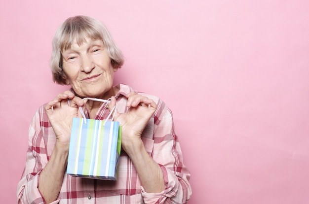 Estilo de vida e conceito de pessoas: feliz mulher sênior com sacola de compras sobre fundo rosa