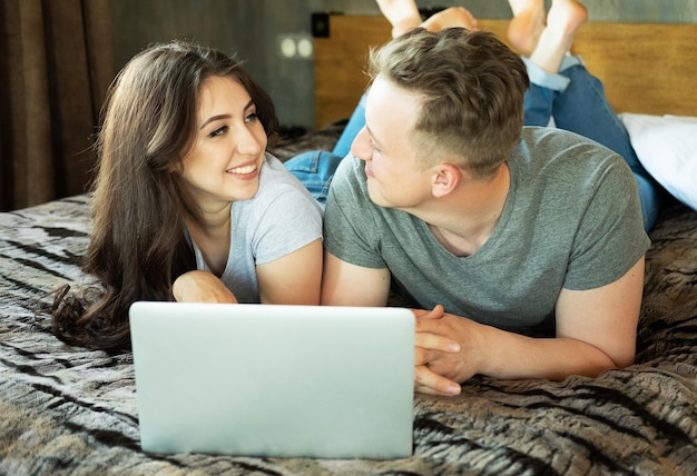 Estilo de vida e conceito de pessoas Jovem casal deitado na cama em casa e usando laptop