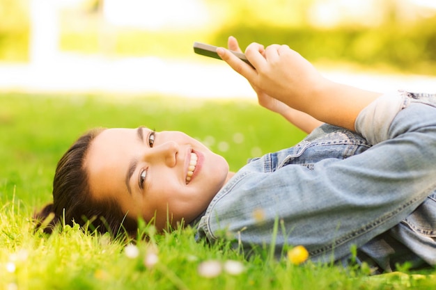 estilo de vida, férias de verão, tecnologia, lazer e conceito de pessoas - jovem sorridente com smartphone deitado na grama no parque