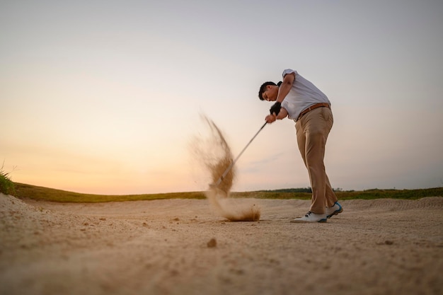 Estilo de vida, golfe, atividade, atividades ao ar livre, esporte, conceito de jogador de golfe Um homem está jogando golfe na areia de um campo de golfe ao pôr do sol no verão. Conceito de estilo de vida do esporte.