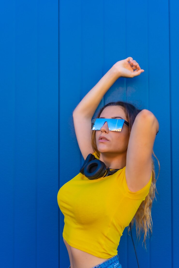 Foto estilo de vida, loira caucasiana com camiseta amarela. mulher jovem posando com fones de ouvido musicais e óculos de sol