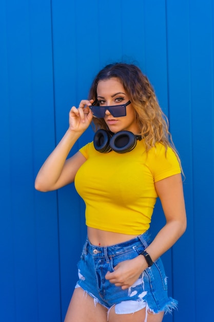 Estilo de vida, loira caucasiana com camiseta amarela. mulher jovem posando com olhar sensual com fones de ouvido musicais e óculos de sol