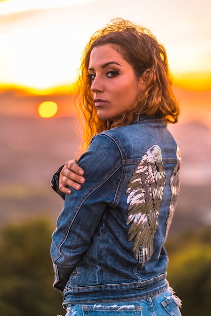 Estilo de vida menina caucasiana em uma jaqueta jeans e shorts jeans Em um lindo pôr do sol de verão