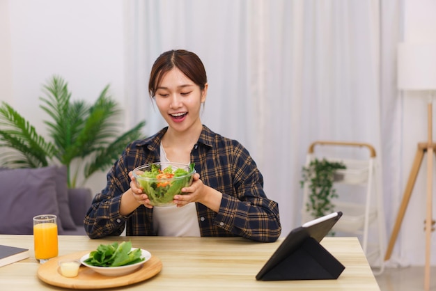 Estilo de vida no conceito de sala de estar jovem asiática animada enquanto segura uma tigela de salada de legumes