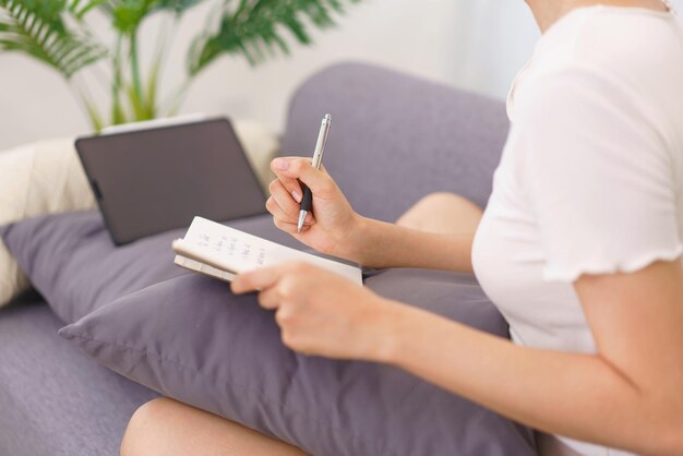 Estilo de vida no conceito de sala de estar Jovem asiática escrevendo dados no notebook enquanto está sentada no sofá