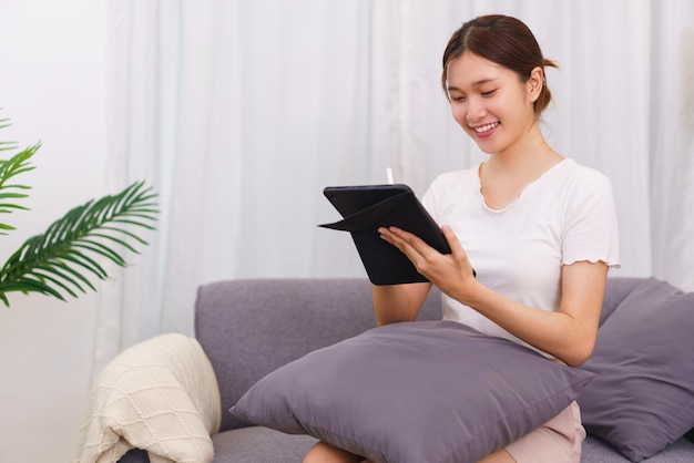 Estilo de vida no conceito de sala de estar Jovem asiática escrevendo dados no tablet enquanto está sentada no sofá