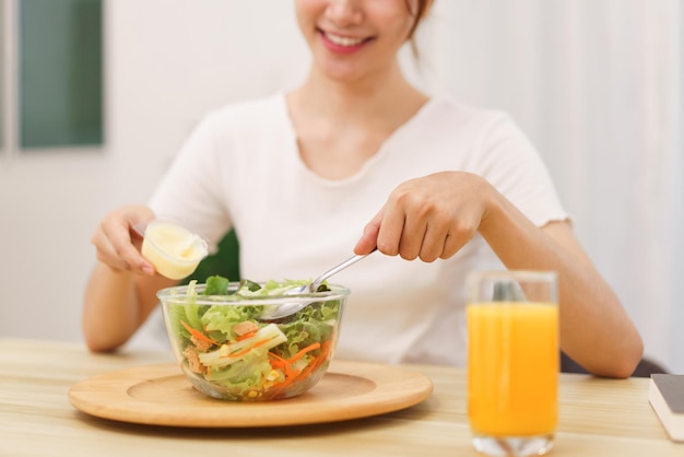 Estilo de vida no conceito de sala de estar jovem asiática misturando salada de legumes com molho de salada