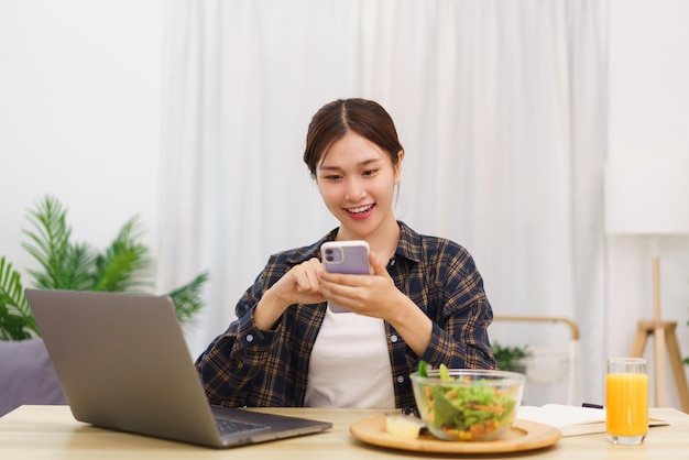 Estilo de vida no conceito de sala de estar Jovem asiática usando smartphone e comendo salada de legumes