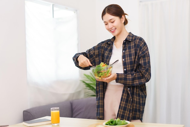 Estilo de vida no conceito de sala de estar Jovem mulher asiática em pé para misturar salada de legumes na tigela