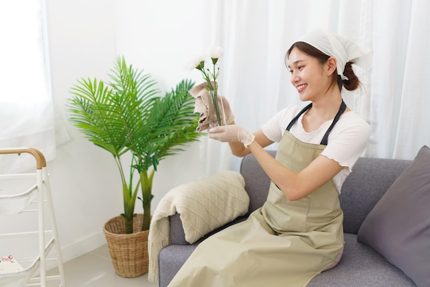 Estilo de vida no conceito de sala de estar Jovem mulher asiática na luva usando pano para limpar vaso de flores