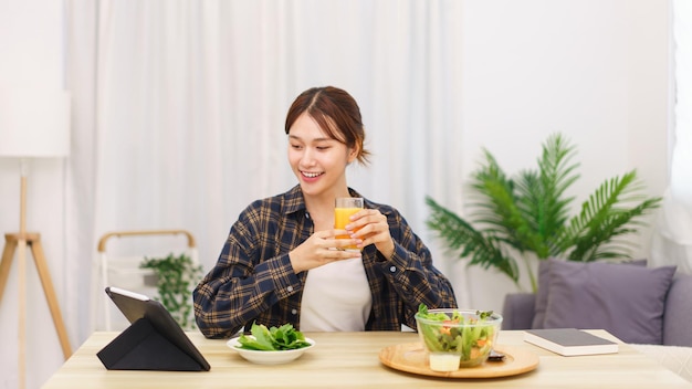 Estilo de vida no conceito de sala de estar Mulher asiática assistindo filme em tablet e bebendo suco de laranja