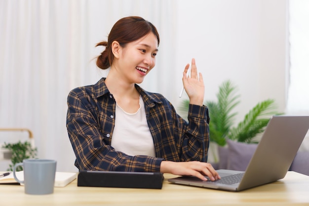 Estilo de vida no conceito de sala de estar Mulher asiática faz gesto de saudação com colega em videochamada