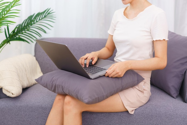 Estilo de vida no conceito de sala de estar Mulher asiática sentada no sofá e usando laptop para navegar nas mídias sociais