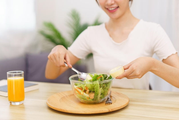 Estilo de vida no conceito de sala de estar mulher asiática usando colher para colocar molho de salada na tigela de salada