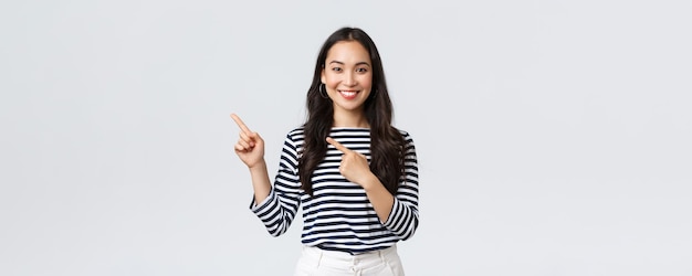 Estilo de vida pessoas emoções e conceito casual Bonita jovem coreana feminina anuncia produto sorrindo câmera animada e apontando os dedos canto superior esquerdo no banner promocional