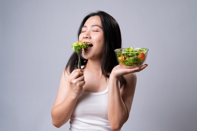 Estilo de vida saudável com conceito de comida limpa. Mulher asiática feliz comendo salada isolada sobre uma parede branca.