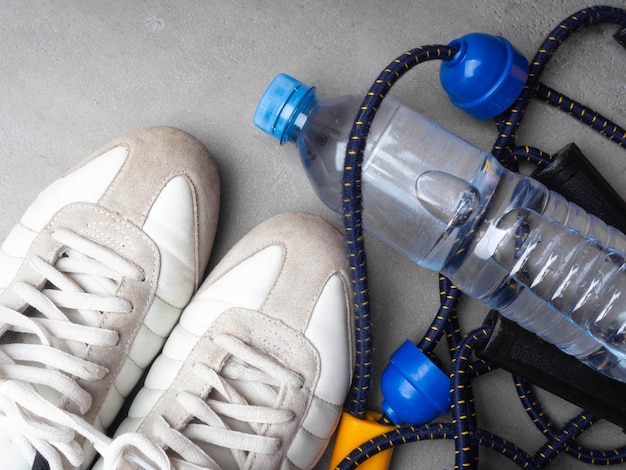 Estilo de vida saudável e conceito de esporte Expansor de tênis branco e garrafa de água em um fundo cinza