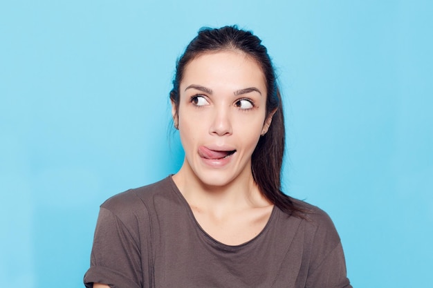 Foto estilo de vida saudável felicidade e conceito de pessoas bela mulher sorridente em fundo azul garota emocional bela modelo moderno mostra língua mulher positiva hipster emoções no rosto