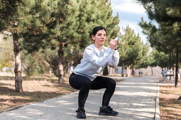 Estilo de vida saudável. mulher atraente alegre fazendo exercícios e se estende em um parque com pinheiros de manhã