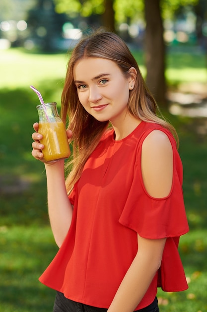 Estilo de vida saudável. Mulher jovem irreconhecível com smoothie de desintoxicação de baga amarela no verão, sobre fundo verde da natureza.