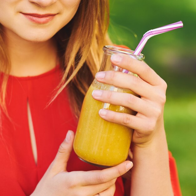 Foto estilo de vida saudável. mulher jovem irreconhecível com smoothie de desintoxicação de baga amarela no verão, sobre fundo verde da natureza.