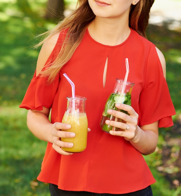 Estilo de vida saudável. Mulher jovem irreconhecível com smoothie de desintoxicação de frutas no verão, sobre fundo verde da natureza