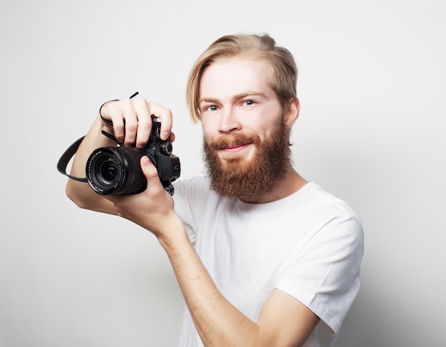 Estilo de vida, tecnologia e conceito de viagens: homem barbudo vestindo uma camiseta branca com uma câmera digital isolada em um fundo branco
