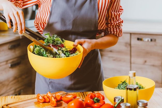 Estilo de vida vegetariano Foto recortada de mulher cozinhando salada de mistura com ingredientes orgânicos frescos em tigela amarela