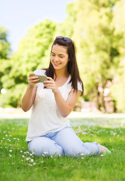 Estilo de vida, verão, férias, tecnologia e conceito de pessoas - jovem sorridente com smartphone sentado na grama no parque