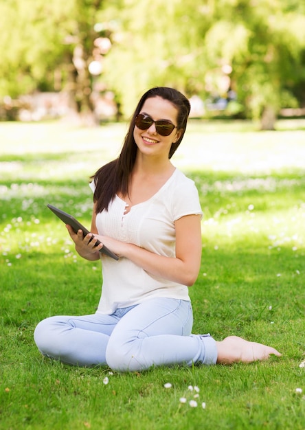 estilo de vida, verão, férias, tecnologia e conceito de pessoas - jovem sorridente com tablet pc sentado na grama no parque