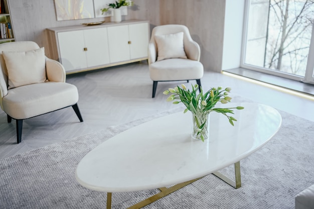 Estilo escandinavo, brillante, clásico, moderno, lujoso, blanco, sala de estar con mesa de mármol, muebles nuevos y elegantes, cómoda, sillones acogedores, plantas de interior. Diseño interior nórdico minimalista.