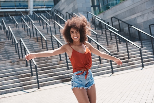 Estilo libre de mujer joven en la calle caminando cerca de escaleras manos un