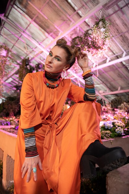 Estilo de moda. Encantado de buena mujer tocando su cabello mientras posa con un vestido naranja