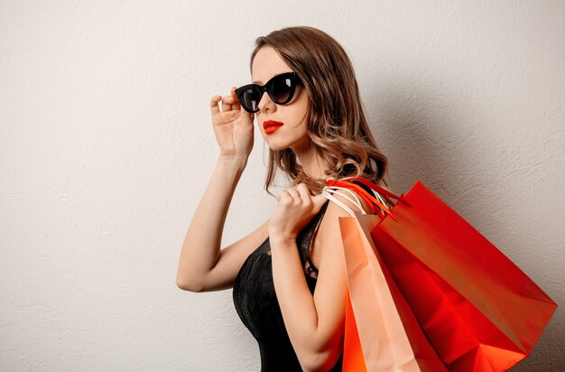 Estilo mujer en gafas de sol con bolsas de compras en la pared blanca