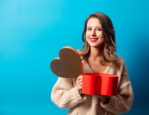 Estilo mujer en suéter con caja de regalo en la pared azul