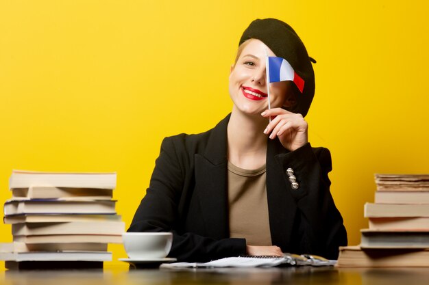 Estilo mulher loira na boina com bandeira francesa e livros em amarelo